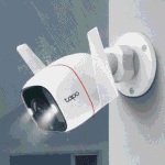 Cámara WiFi exterior Tapo C320WS instalada en una pared bajo la lluvia, con los focos encendidos